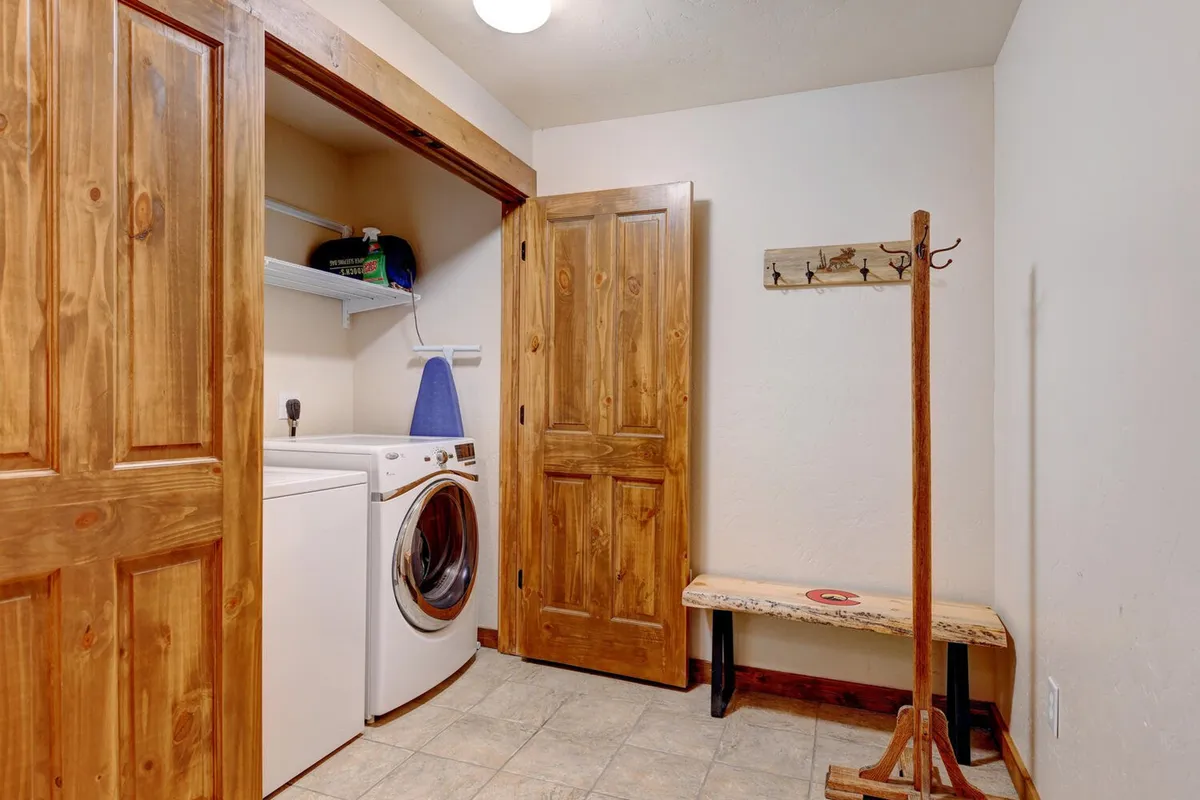 A practical laundry and mudroom area featuring a modern washing machine, wooden bench, and hooks for organizing coats or gear. The space is tidy, welcoming, and clearly designed for managing the aftermath of outdoor exploits—keeping things clean and organized.