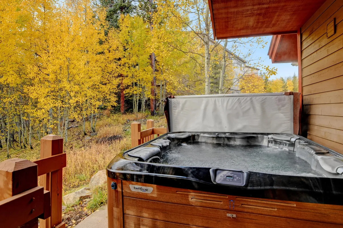 An inviting wooden deck featuring a private hot tub, surrounded by yellow autumn foliage. The deck offers serene views of nature, ideal for a peaceful morning coffee or a relaxing soak after a day of adventure.
