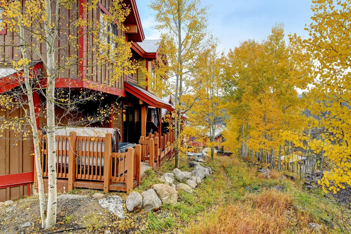 This tranquil exterior shot shows a wooden deck surrounded by colorful fall foliage and a stone pathway inviting guests to explore the natural beauty. The setting feels peaceful and is perfect for watching sunsets, hosting gatherings, or simply soaking in the changing seasons.