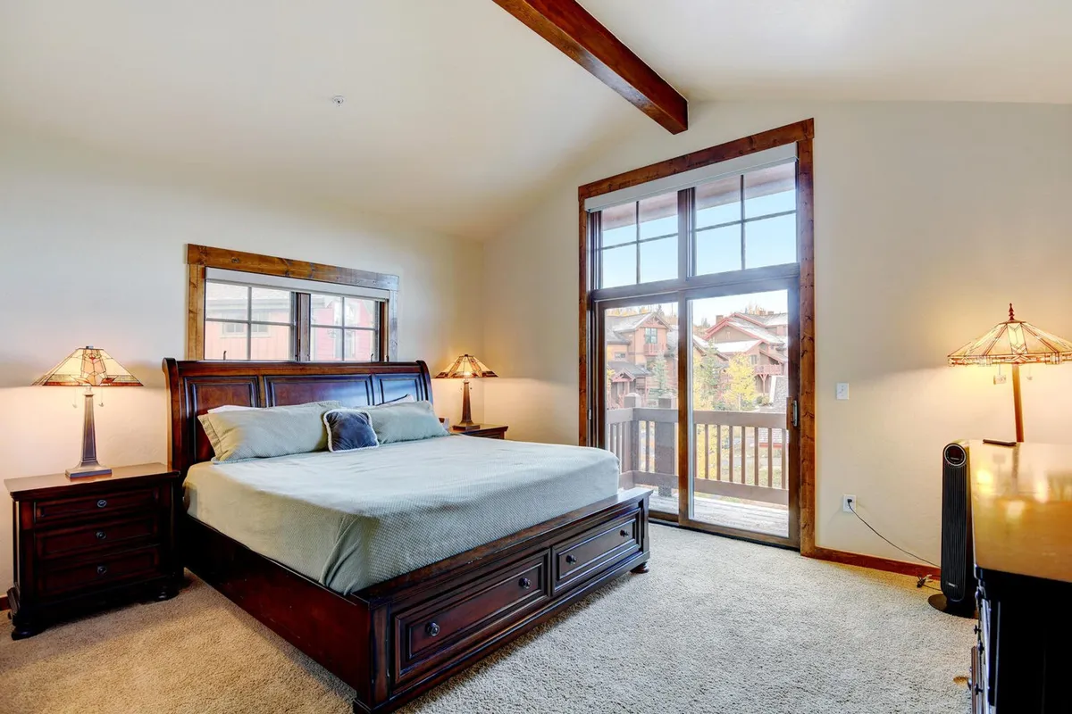 A tranquil king-size bedroom featuring a large, plush bed adorned with premium bedding, flanked by nightstands and lamps. The room is bathed in natural light from expansive windows, and blackout shades ensure restful sleep. The serene decor and cozy atmosphere make it an ideal sanctuary for couples or guests seeking privacy and comfort.