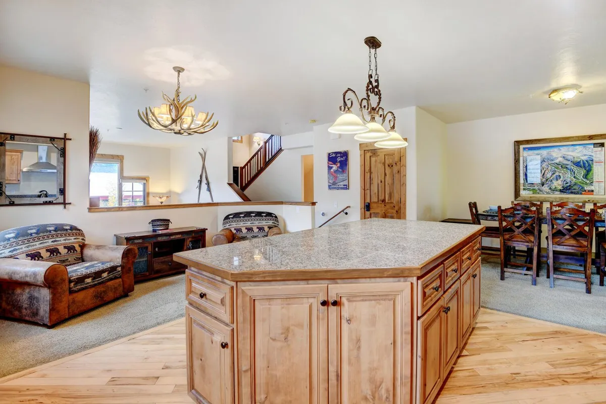 This interior image presents a stylish and friendly kitchen and dining area, featuring a kitchen island, an elegant chandelier, a spacious dining table, and a cozy seating area. The ambiance is inviting and perfect for family gatherings, entertaining, and relaxed evenings at home.