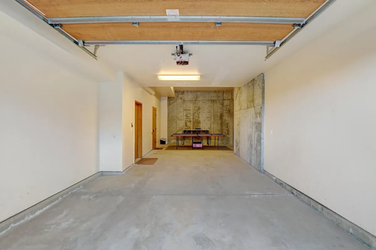 A spacious garage featuring a large garage door, concrete floor, and a ping pong table. The open floor area offers ample space for storing outdoor gear, bikes, and adventure equipment, while the presence of the ping pong table hints at recreational possibilities beyond storage.