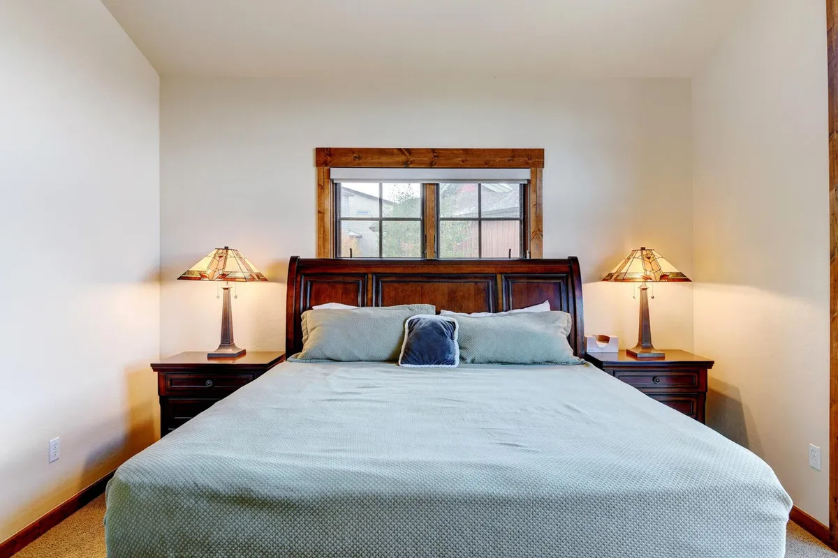 A serene bedroom scene with a comfortable bed, soft linens, elegant nightstands, warm lamps, and a window letting in gentle morning light. The uncluttered design and tranquil color palette enhance the sense of peaceful retreat and privacy.