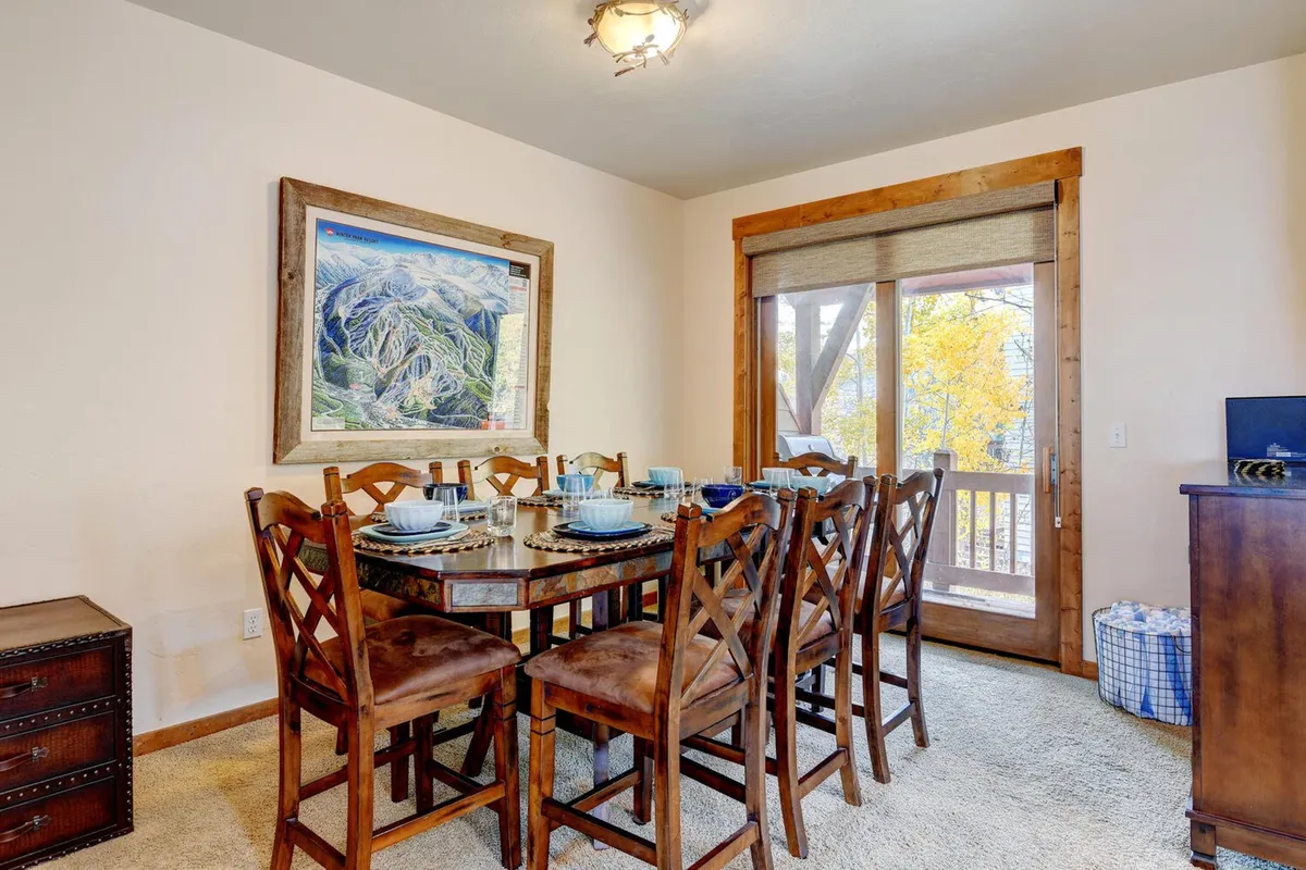A stylish dining area centered around a wooden table set for a meal, with large artwork on the wall and a sliding wooden door leading out to the patio. The space feels welcoming and ideal for family dinners or celebrations, seamlessly connecting to the outdoors.